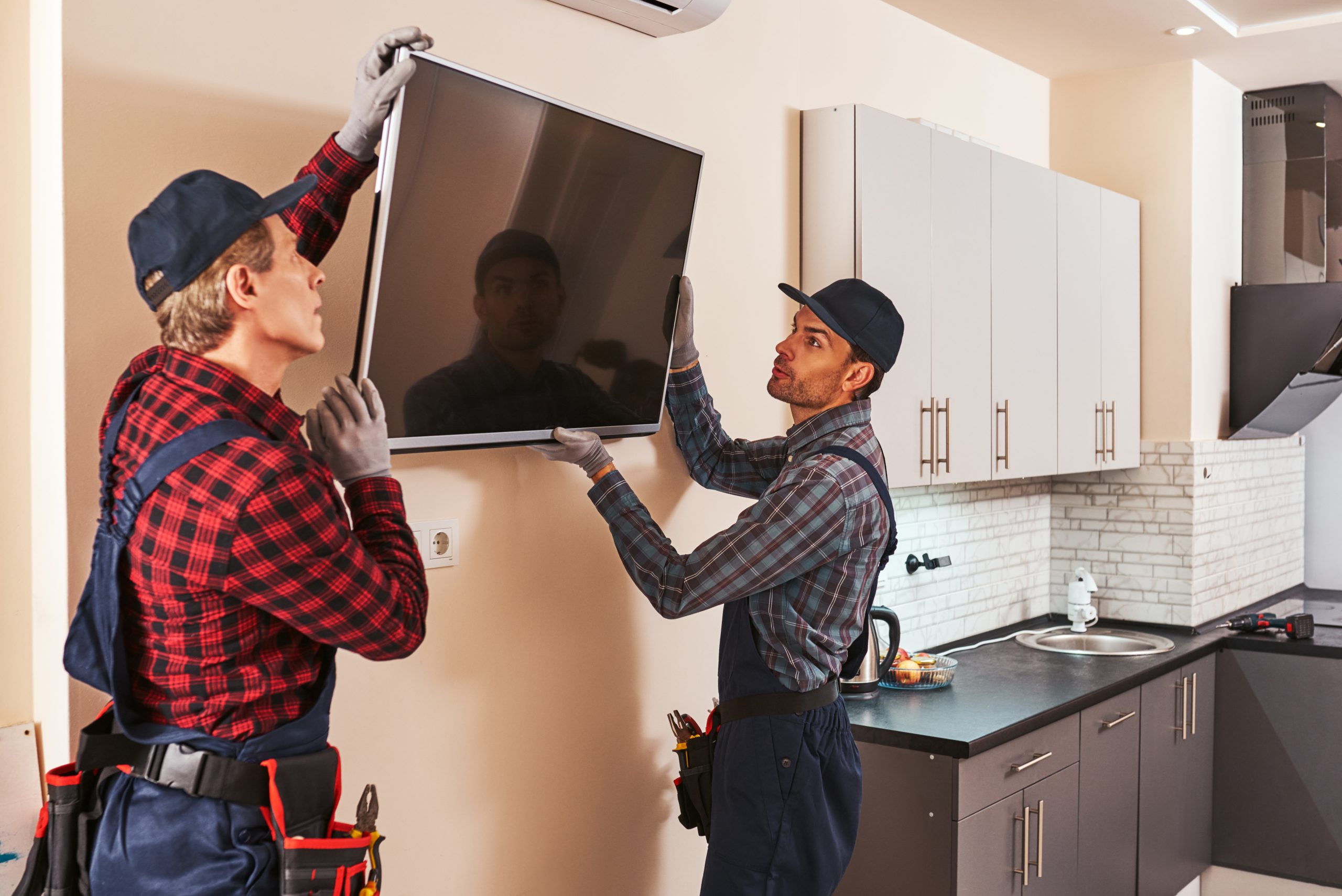 Trained handyman in Dubai installing a wall-mounted TV while a family watches, with neatly arranged tools and a spotless finish.