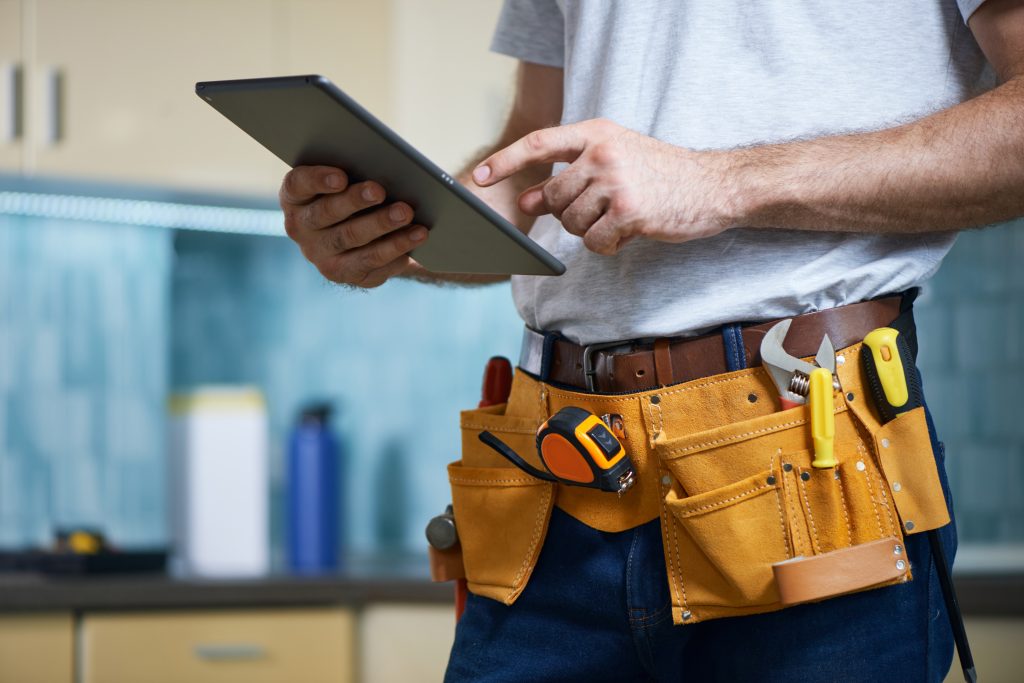 Handyman in UAE holding a tablet with service schedule, background featuring UAE landmarks, ready for fast, affordable handyman services.