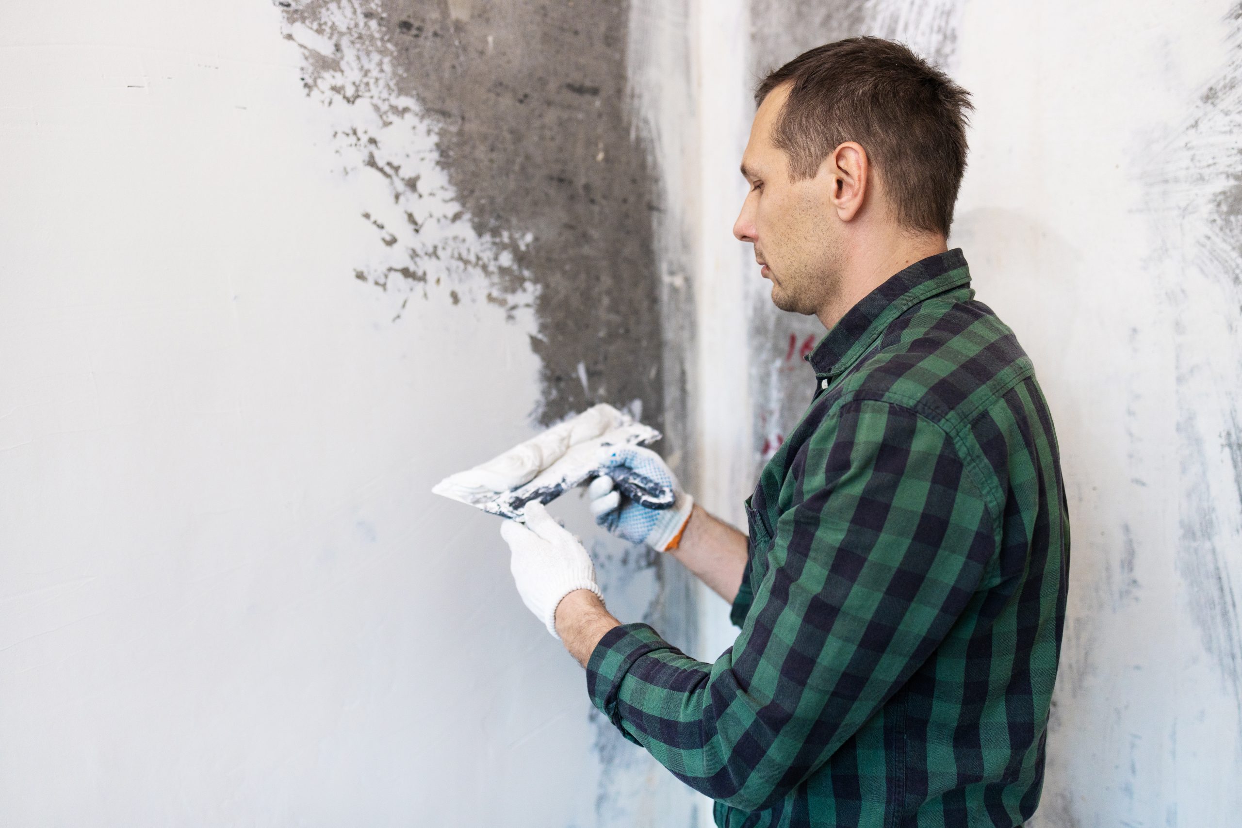 Painter filling cracks and smoothing a wall before painting in Dubai, with protective coverings on nearby furniture for professional surface preparation.
