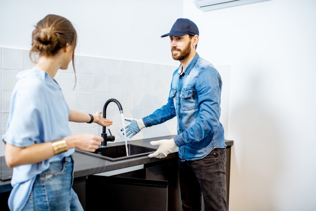 Smiling plumber in Dubai showing a satisfied customer a repaired faucet with clean water running, symbolizing trusted plumbing services.