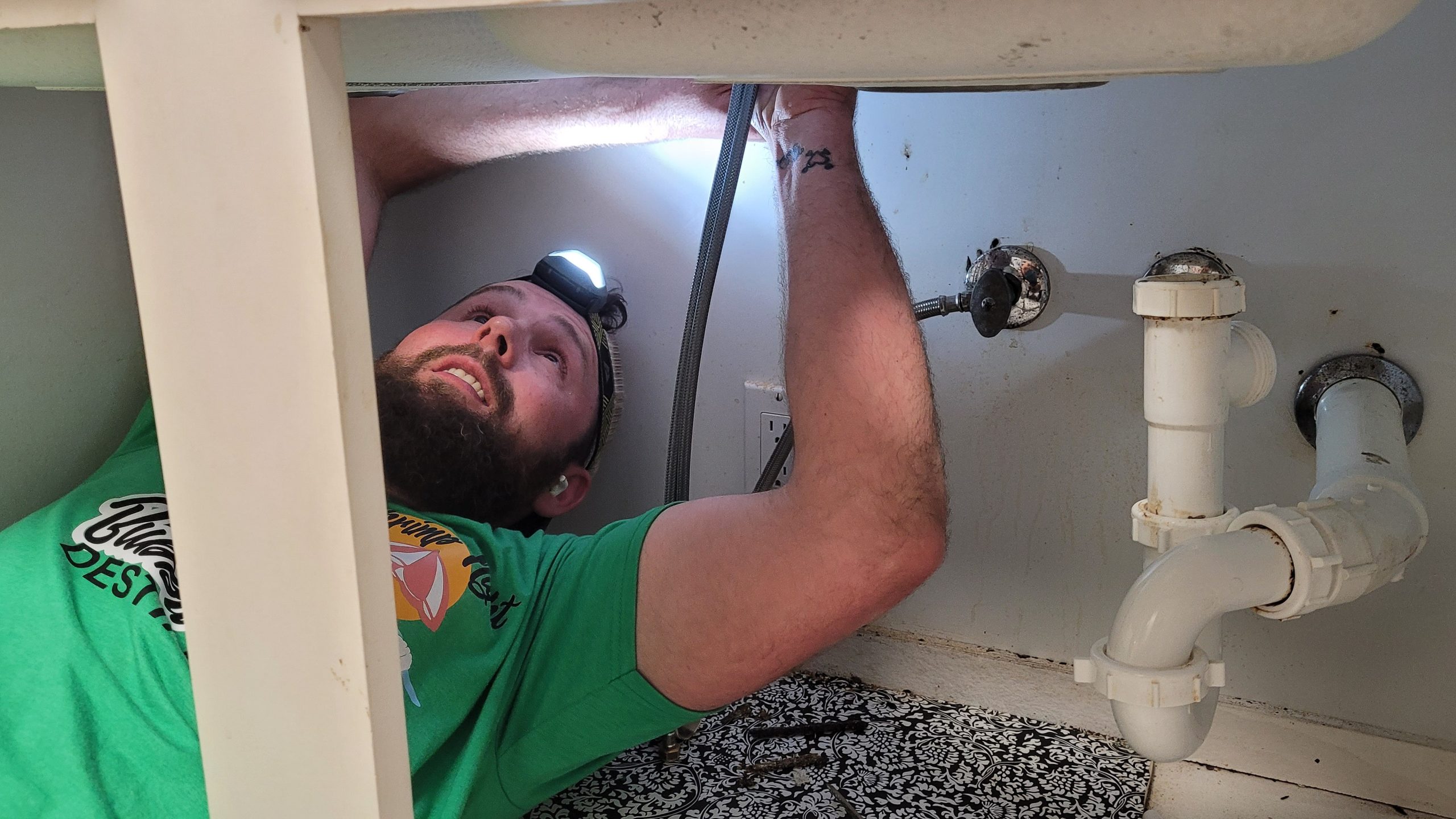 Dubai plumber inspecting under-sink pipes with a flashlight and leak detection device, identifying water leaks and plumbing issues.