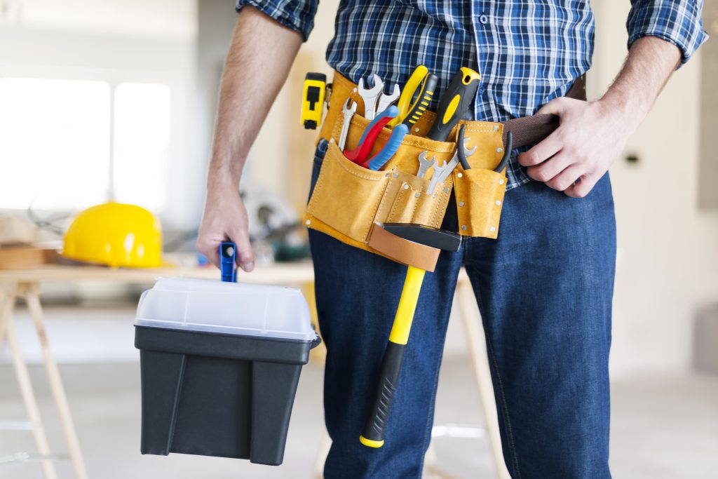 Smiling handyman in Abu Dhabi holding a toolbox inside a clean home interior, ready for professional repair and maintenance services.