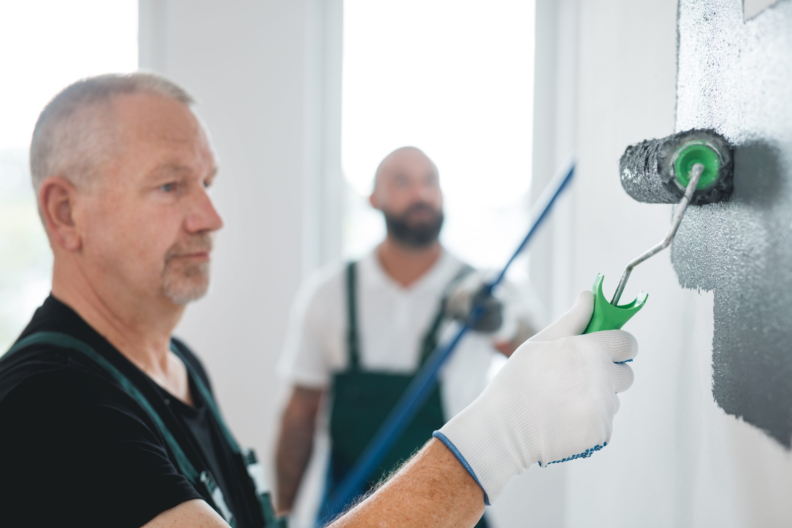 Two painters in Dubai applying paint with rollers and brushes on protected floors, using professional-grade materials for even, long-lasting coverage.