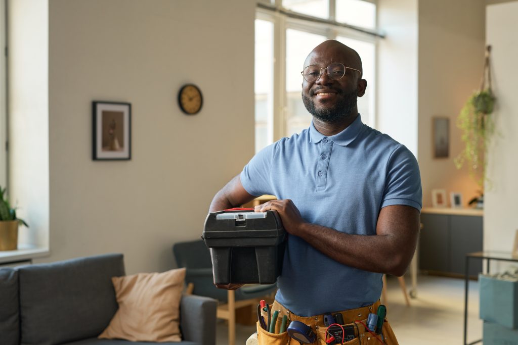 Friendly handyman in Sharjah smiling beside toolbox in a bright living room, ready for reliable repair services.