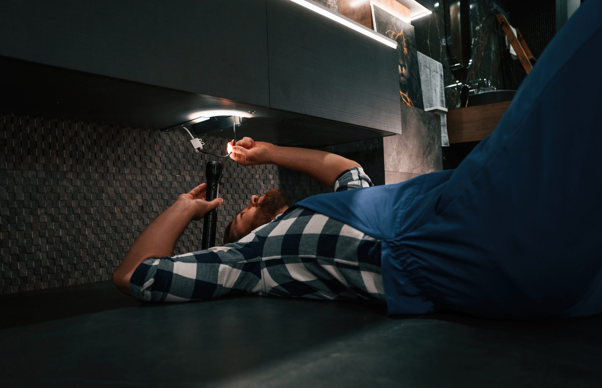 Pipe repair services Dubai - professional plumber inspecting under-sink pipes.