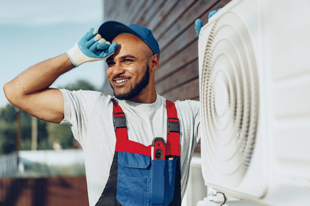 Smiling AC coil cleaning Abu Dhabi technician with cleaning equipment beside an open AC unit, ready to deliver affordable AC maintenance.
