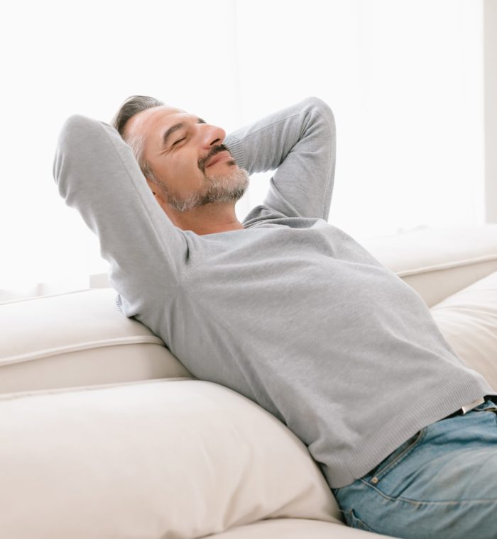 Relaxed man enjoying rest lying on comfortable couch with the ha Relaxed man enjoying rest lying on comfortable couch with the hands on the head in living room at home. Calm middle-age man breathing fresh air enjoying no stress free peaceful weekend in house.