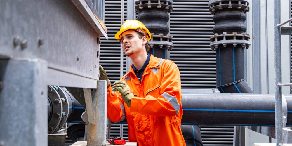 AC coil cleaning Abu Dhabi technician in protective gear brushing condenser coils outdoors as part of emergency HVAC service.